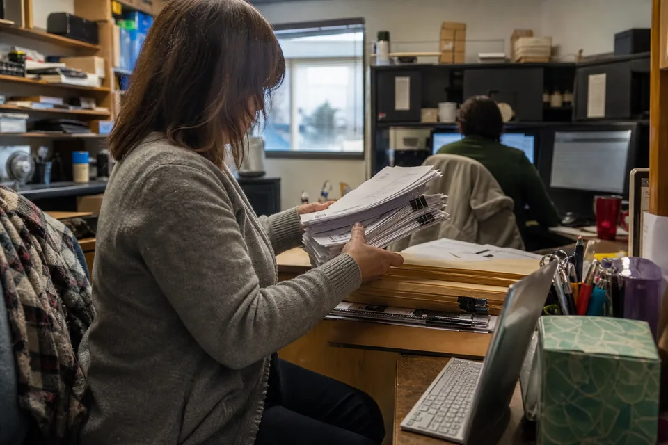 Bookkeeper sorting a stack of printed monthly client report packets into folders