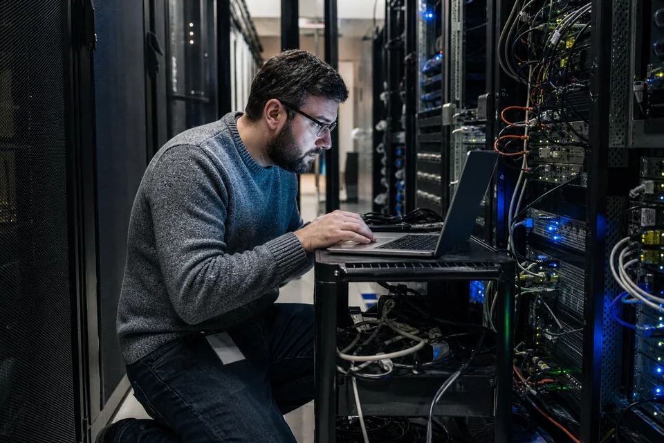 Database administrator with a laptop in a server room aisle